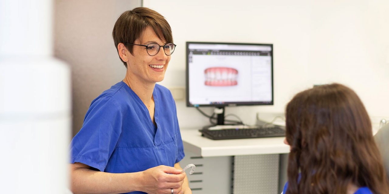 Zahnärztin Dr. Mairock lächelnd vor einem Computer-Monitor während einer Patientenberatung